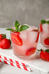 Glass of cold cocktail with strawberry on white tile table near grey wall, closeup