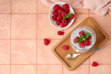 Glass of tasty chia seed pudding with fresh raspberries and mint on beige tile background