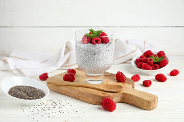 Glass of tasty chia seed pudding with fresh raspberries and mint on white wooden background