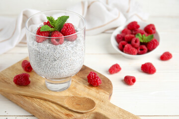 Glass of tasty chia seed pudding with fresh raspberries and mint on white wooden background
