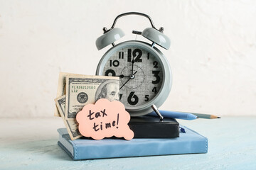 Books with alarm clock, money, stationery and text TAX TIME on grunge blue table near white wall