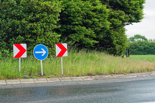 Three road signs two red chevrons and a blue right arrow at a roundabout