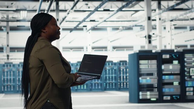 Data center worker using laptop to manage software updates for system stability. African american woman in server room configuring infrastructure for optimum performance, camera B
