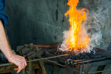 Heating a metal rod in a bright coal fire on the forge