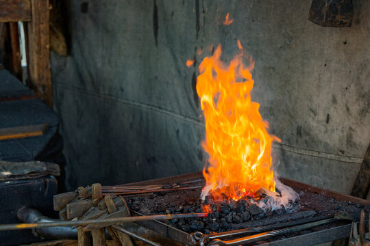 Blazing coal forge by a concrete wall with hanging hammers