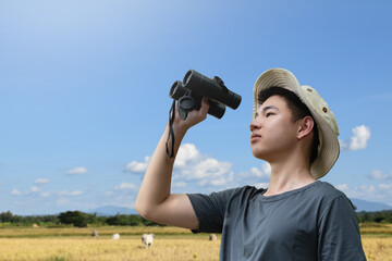 Young man with binoculars exploring the forest on a sunny day, enjoying outdoor adventure and wildlife observation.