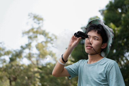 Young man with binoculars exploring the forest on a sunny day, enjoying outdoor adventure and wildlife observation.