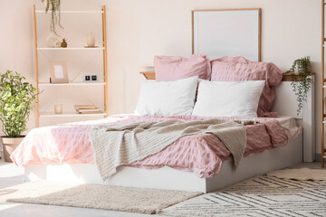 Bed with stylish pink bedding, shelving unit and houseplants in bedroom at home