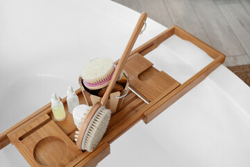 Bucket with different massage brushes and cosmetic products on wooden stand in bathroom, top view