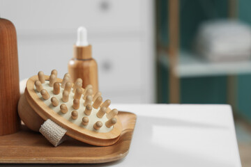 Tray with massage brushes, wooden balls and cosmetic products on table near blue wall in bathroom