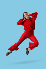 Fototapeta premium Young happy woman in headphones jumping on blue background