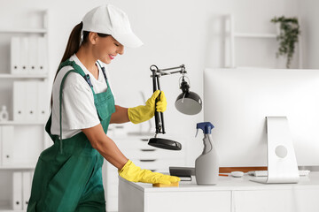 Female janitor cleaning desk in office