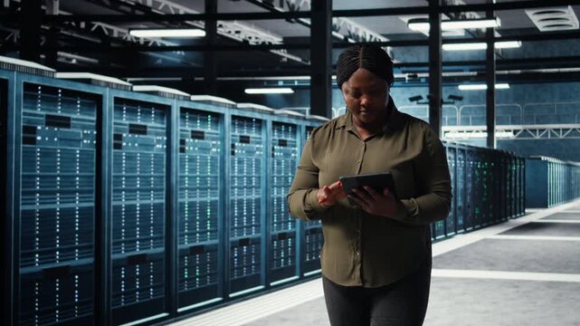 Data center engineer using app on tablet to ensure error free rigs networks for intense computational demands. Worker monitoring server hub equipment components for failures, camera A
