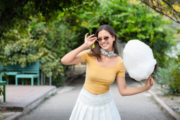 Beautiful young happy woman with cotton candy in park, outdoors