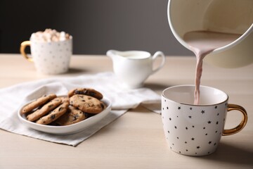 Pouring cocoa into cup near cookies on wooden table