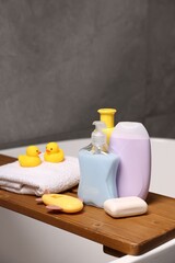 Baby accessories and bathing products on wooden tray in bathtub indoors, closeup