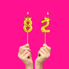 Birthday on a fuchsia background with the number 82 - Hands holding number-shaped candles