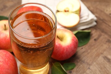 Fresh cider in glass and apples on wooden table, closeup. Space for text