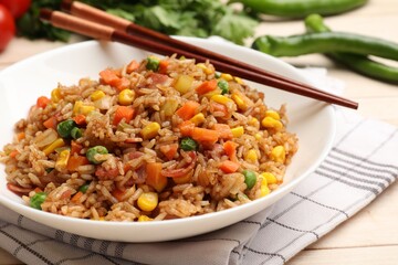 Tasty fried rice and chopsticks on light wooden table, closeup