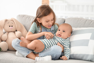 Little girl with her baby brother sitting on sofa at home