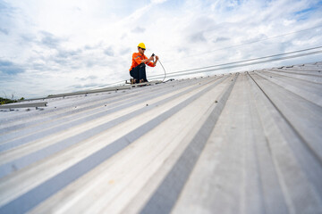 Technician in safety uniform and helmet kneeling on a rooftop, using a drill for precise installation work. A scene highlighting safety, professionalism, and technical expertise in construction.