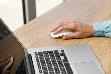Female hand using laptop with computer mouse on table at home, closeup