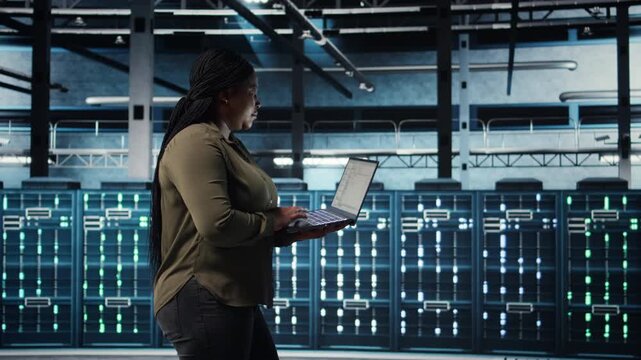 Software developer in data center using laptop to coordinate deployment of new server architecture. Server hub IT professional using notebook to do rollout of cybersecurity framework, camera A