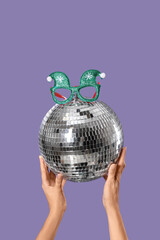 Female hands with disco ball and Christmas decor on lilac background
