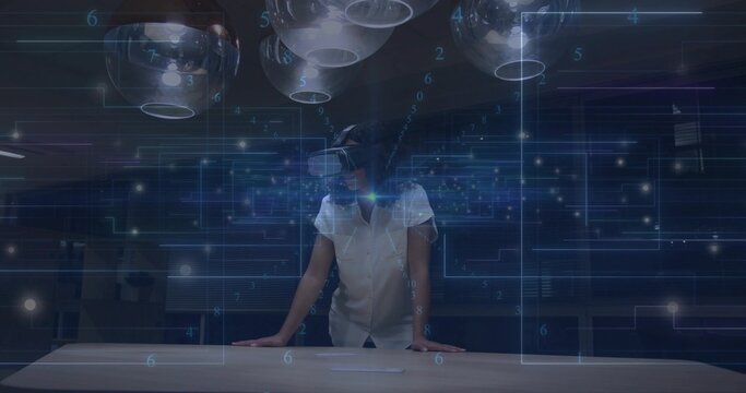 Leaning adult woman wearing VR headset using holographic UI in tech lab, with pendant lights