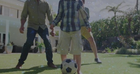 Playing three-generation family kicking soccer ball in suburban backyard, with fence, palm tree