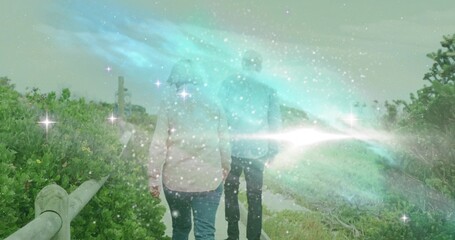 Walking couple wearing jeans on coastal trail with wooden railing and vegetation, ethereal lights