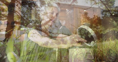 Leaning woman watering plants in planter box in backyard, wearing apron, holding metal watering can