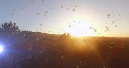 Casting glowing sun illuminating scrubby trees, rolling hills at hillside, with lens flare sparkles