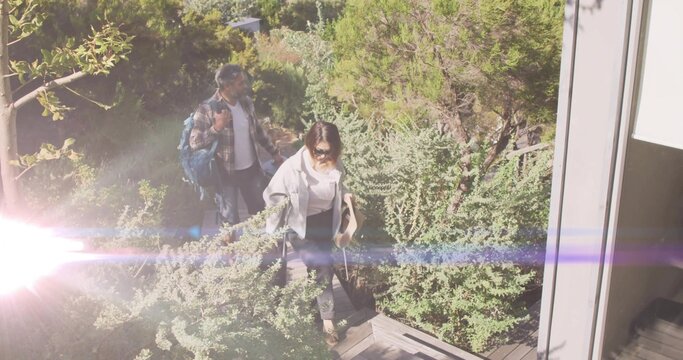 Walking couple ascending wooden pathway at entrance, carrying backpack and tote bag with rolled mat - Powered by Adobe