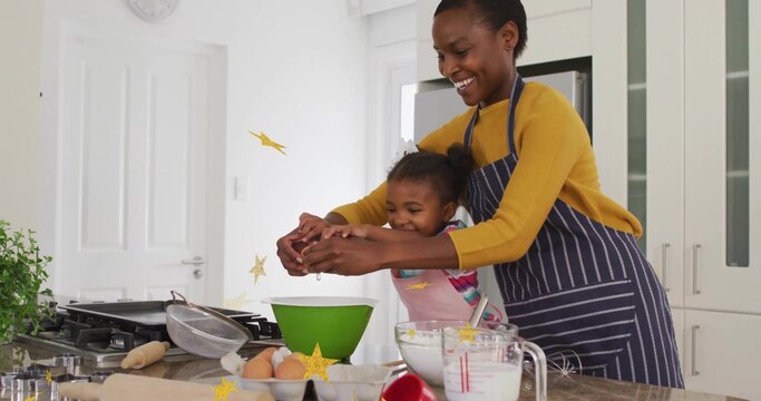 Guiding mother and daughter wearing aprons cracking egg over kitchen island, with green mixing bowl - Powered by Adobe