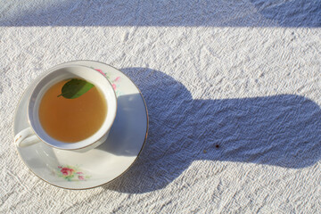 Hot tea with mint leaf in white luxury cup on wooden tray under sunlight. Morning breakfast for...