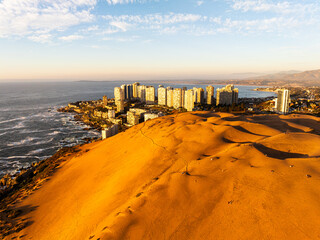 An aerial shot of Concón's sun-drenched dunes and coastal city, with people visible on the sandy landscape.