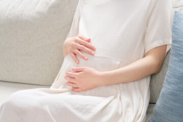 ソファーに座ってお腹を触る妊婦　顔無し