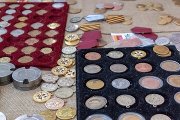 A diverse collection of vintage coins, medals, awards and banknotes displayed on a textured surface for collectors