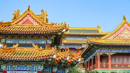 Naklejka premium Traditional Chinese temple in Penglai, Shandong, with red pillars, golden roofs, and ornate details, surrounded by lush greenery and a serene natural setting.