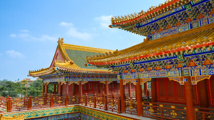 Naklejka premium Traditional Chinese temple in Penglai, Shandong, with red pillars, golden roofs, and ornate details, surrounded by lush greenery and a serene natural setting.