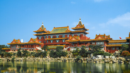 Fototapeta premium Traditional Chinese temple in Penglai, Shandong, with red pillars, golden roofs, and ornate details, surrounded by lush greenery and a serene natural setting.