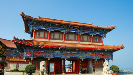Obraz premium Traditional Chinese temple in Penglai, Shandong, with red pillars, golden roofs, and ornate details, surrounded by lush greenery and a serene natural setting.