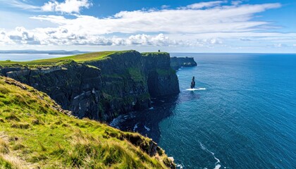 Dramatic coastal cliffs meet a vibrant blue ocean under a partly cloudy sky. Lush green grass tops the cliffs
