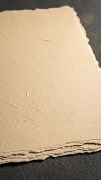 Stack of Beige Handmade Paper with Deckle Edges on a Dark Gray Textured Surface in Soft Lighting