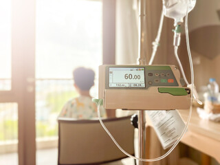 Medical infusion pump with digital screen displaying flow rate in a hospital room. Pediatric patient resting in bed in the background. Healthcare and intravenous therapy concept.