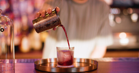 Serving drink. Preparing liquor. Bartender pouring red strained liquid from metal shaker. Professional making refreshing beverage.