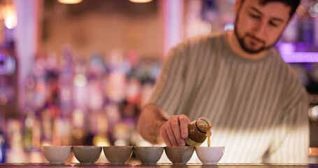 Barman pouring liquid. Asian pub. Bartender filling portioned small ceramic cups for sake. Man serving traditional japanese alcoholic order.