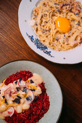 Traditional cuisine. Dinner meal. Carbonara with egg yolk served on wooden table. Tomato paella with scallop in creamy saffron sauce.