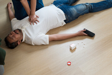 Emergency CPR on unconscious man lying on floor after collapse with medicine pills and phone nearby